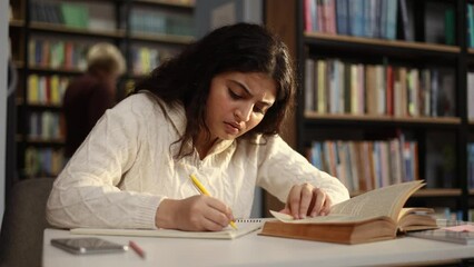 Tired student girl feeling upset during study writing in textbook at university library Stressed curly young woman exhausted from remote distance work or education and hard program indoors - Powered by Adobe