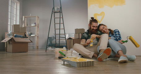 Newlywed caucasian couple is renovating their new home, painting the walls and positively smiling -...