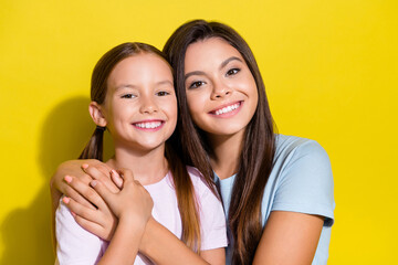 Photo of charming sweet little sisters wear t-shirts cuddling smiling empty space isolated yellow...