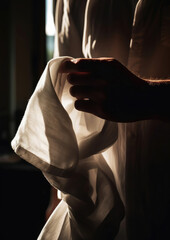 Man holding white fabric, bathed in sunlight by the window, creating a tranquil and timeless moment