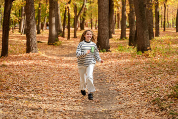 Fototapeta premium A beautiful teenage girl with long hair smiles and runs in an autumn park. Togliatti, Russia - 30 Sep 2023