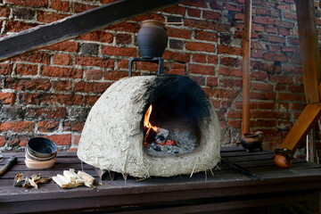 A close up on a temporary furnace made out of clay used for making pots and baking cakes spotted on a wooden table and located next to a wall made out of red brick in summer in Poland