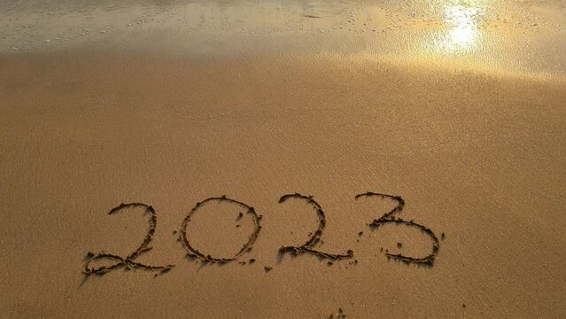 2023 written on the sand washed away by the wave at sunset