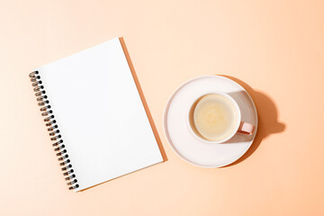 Coffee in cup and spiral notebook on Peach Fuzz background with sharp shadows. Top view, flat lay,...