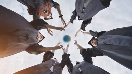 Fototapeta na wymiar College alumni students toss a globe of the world into the sky.