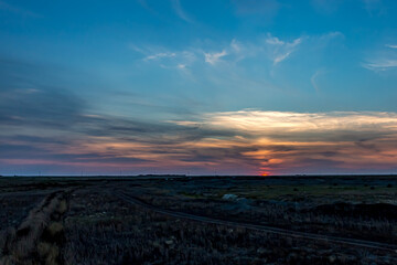 Sunrise or sunset in the Russian steppe at golden hour. Cumulostratus Cirrocumulus, Altocumulus and Stratocumulus clouds. The sun is shining from behind a cloud. Red orange and white shades.