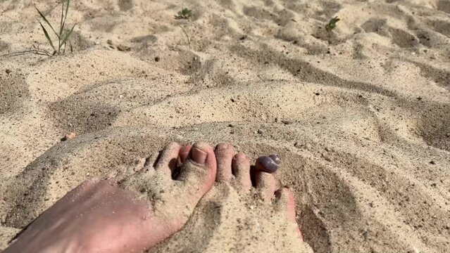 women's feet are buried in the river sand on the beach in summer