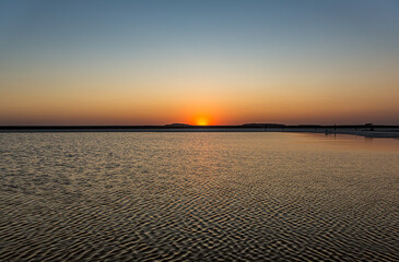 Fototapeta premium Sunset or sunrise on salt lake Baskunchak (Russia). Bright sun in a cloudless sky, calm brine in the saline. Morning or evening in summer, autumn or spring.