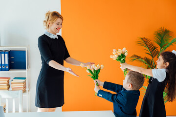 Schoolchildren giving flowers to teacher for holiday in classroom
