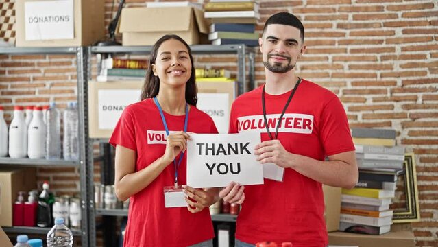 Confident young man and woman volunteers, standing in unity at charity center, holding a heartfelt 'thank you' paper banner in spotlight of altruism.