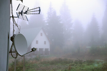 Autumn rural landscape with satellite dish and house on background of foggy forest