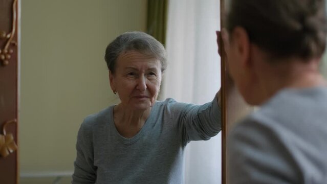 Satisfied smiling old lady looking at herself in the mirror