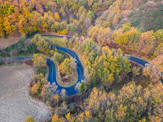 Italy, 08 December 2023 - aerial view of a hairpin road in the middle of a forest with autumn colors