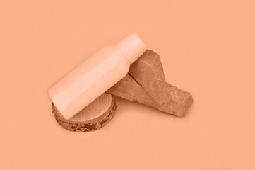 Peach fuzz is color of year 2024, tinted image. A white plastic jar of cosmetic product stands on a stone podium flowers on a pink background. Bio cosmetics mock up
