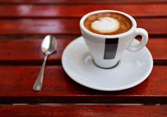 americano cup on saucer with spoon, ashtray, glass of water on red wooden coffee shop table (espresso, milk, macchiato) european style (cappuccino)