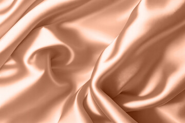Abstract background, folds of silk fabric in peach fuzz color.