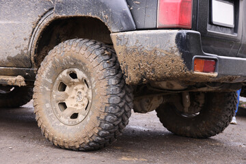 Wheel closeup in a countryside landscape with a mud road. Off-road 4x4 suv automobile with ditry body after drive in muddy road area