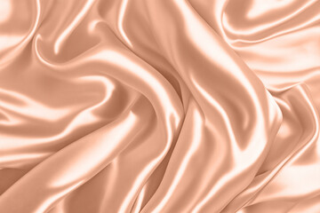Abstract background, folds of silk fabric in peach fuzz color.