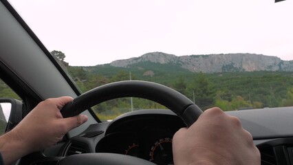 Man drives car along empty freeway road to distant old cliffs closeup. Man drives modern car across highland on interesting journey. Man driver controls car travelling to rocky mountains on vacation