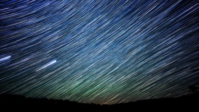 Time lapse of colorful star trails rotating through the night sky above a silhouette of trees. The effect was created by stacking and blending multiple clips of the same night scene.