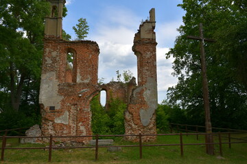 Close up on abandoned ruins of a castle, church, cathedral or shrine made out of red brick and located next to a Christian cross seen next to a forest or moor on a sunny summer day in Poland