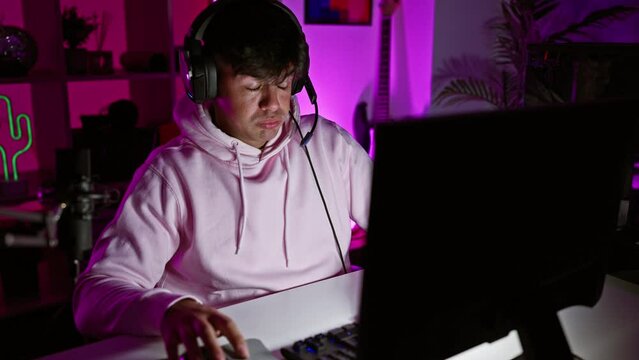 Exhausted young hispanic man, a bored streamer, yawning while gaming at night. gamer guy playing video game in dark gaming room, streaming live on computer with headset and microphone on.