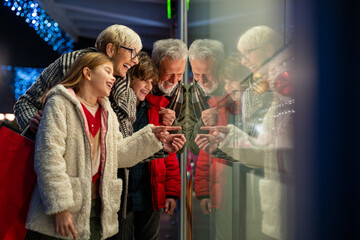 Happy smiling children choosing Christmas presents with grandparents wearing warm clothing standing...