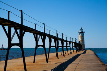 Fototapeta na wymiar Industrial Pier Leading to White Lighthouse Under Clear Blue Sky in Michigan
