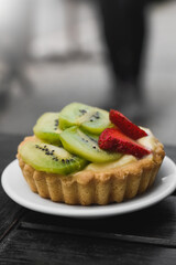 fruit tart with kiwi and strawberry on top of a plate in the foreground, space for copying