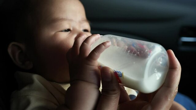 Baby girl drinking formula milk in bottle, mother feed her infant