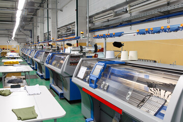 A row of industrial textil flat knitting machines in a knitwear factory.