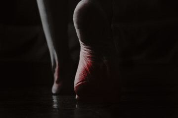 The feet of a girl on the floor of the house are highlighted in red in the dark, black and white photo, pain in the legs, women's bare feet on the floor