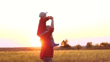 Farmer dad carries infant boy on shoulders. Farmer dad wanders through wheat field with child sitting atop shoulders. In expanse of wheat farmer family delights in stroll together at sunset on horizon - Powered by Adobe