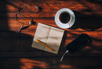 Paper notebook and black smartphone with empty screen, pen, headphone and cup of coffee lies on a...