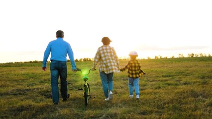 Mum and dad with youngster enjoy stroll with bike in nature. Inquisitive kid explores hidden trails of countryside with parents on sunny day. Active family weekend in rural area during summer season