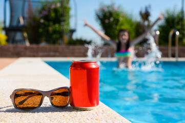 Red can of drink by the pool. The concept of a summer holiday at a resort.