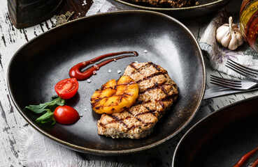 Grilled pork chop steak with tomatoes and spices on plate over rustic wooden background. Meat Dishes, top view, close up