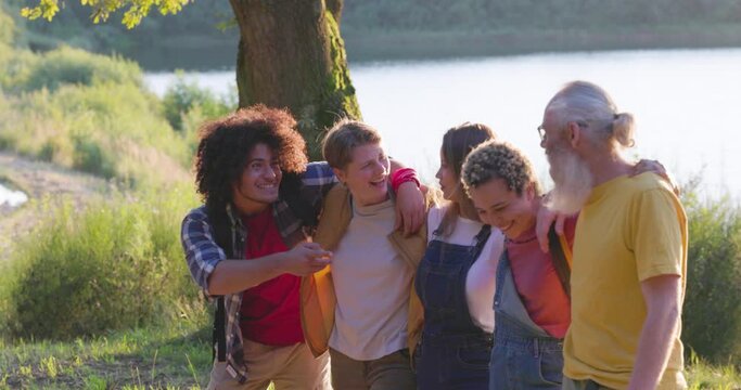 This vibrant image captures a group of friends of diverse ages and backgrounds in a spontaneous display of laughter and affection by a lake. The warm glow of sunlight filters through the scene