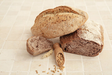 Loaves of fresh bread and scoop with wheat grains on beige tiled table