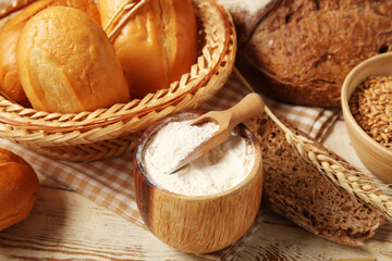 Loaves of different fresh bread with wheat spikelets and flour on white wooden background