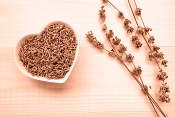 Dried lavender flowers in a bowl on a wooden background. Top view, place for text. Peach fuzz is color of year 2024.