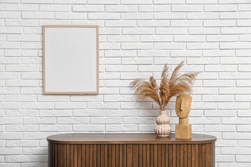 Modern brown chest of drawers with pampas grass in vase and photo frame near white brick wall in...