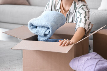 Young woman putting folded sweater in box at home, closeup