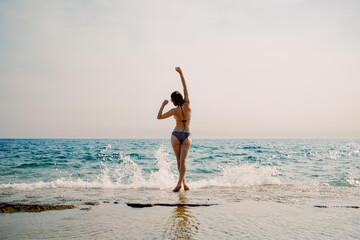 A joyful moment captured as a woman dances on the beach, with the sparkling sea as a perfect...