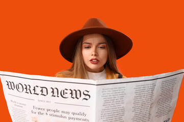 Young woman reading newspaper on orange background, closeup