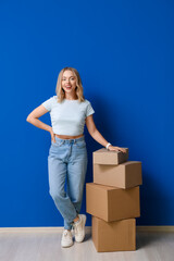 Happy young woman with cardboard boxes on blue background
