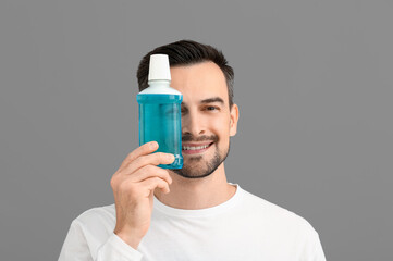 Handsome man with mouth rinse on grey background, closeup