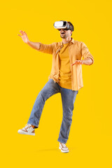 Young man in VR glasses on yellow background