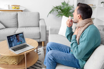 Ill young man using spray for sore throat while video chatting with doctor on laptop at home