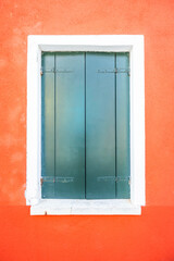 A windows with closed green shutters and a white frame on a bright red wall